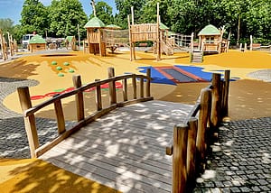 Une structure de jeux en bois sur mesure avec un pont accessible et un trampoline, adaptée aux personnes handicapées.