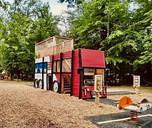 Structure de jeu en bois en forme de bus scolaire avec des jeux ludiques, réalisée par un design studio et placée sur une aire de jeu.