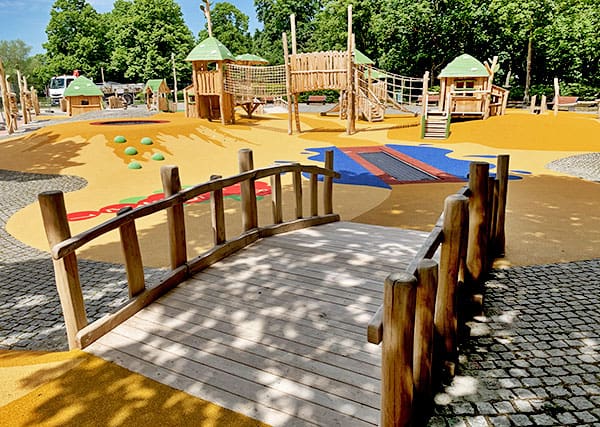 Une structure de jeux en bois sur mesure avec un pont accessible et un trampoline, adaptée aux personnes handicapées.